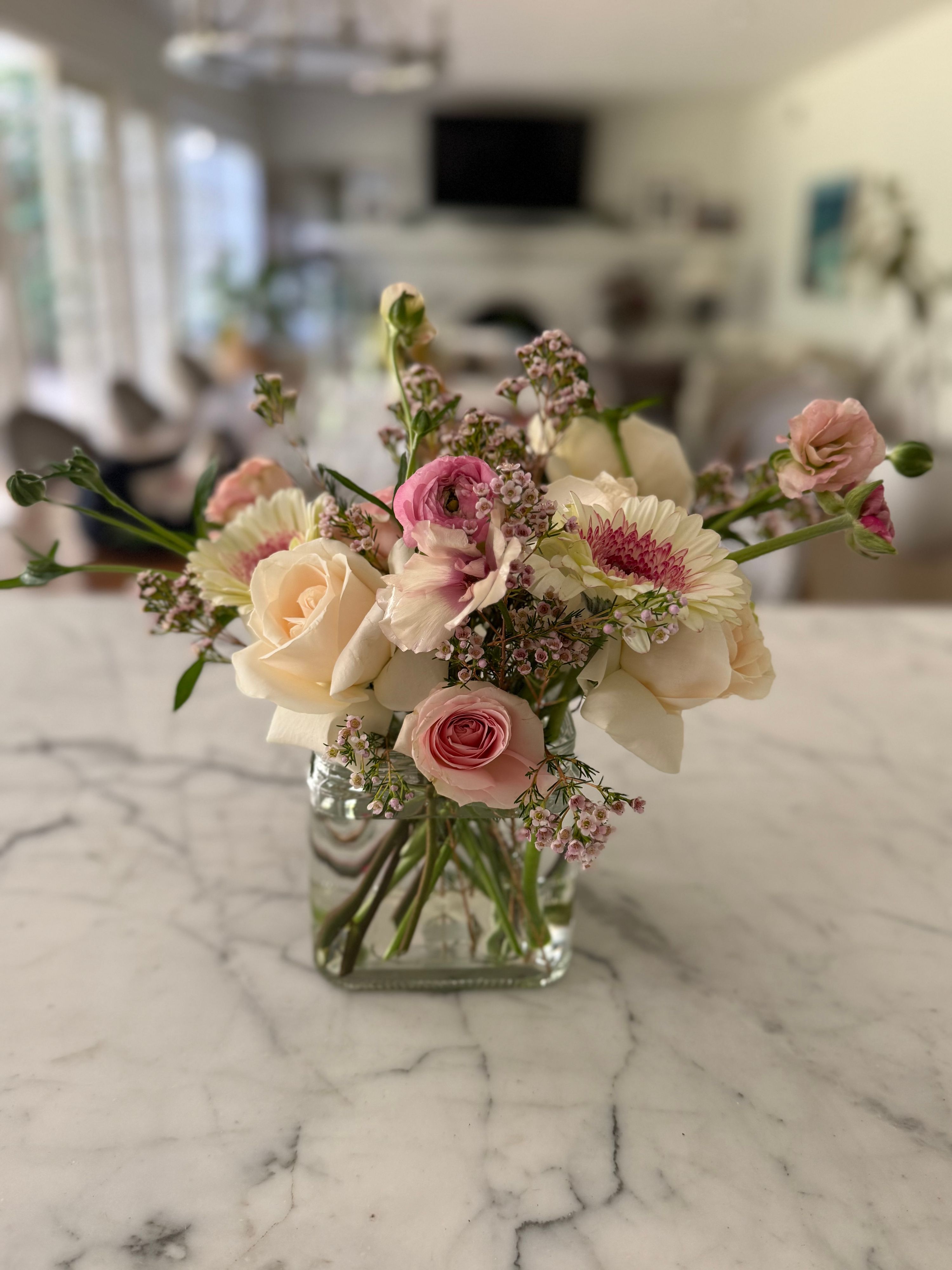 Blush arrangement of cream roses, pink ranunculus and gerbera in a glass cube vase