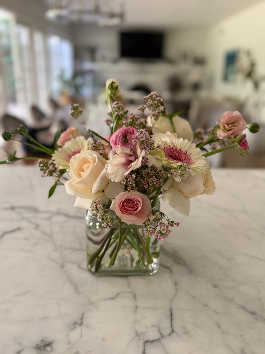 Blush arrangement of cream roses, pink ranunculus and gerbera in a glass cube vase