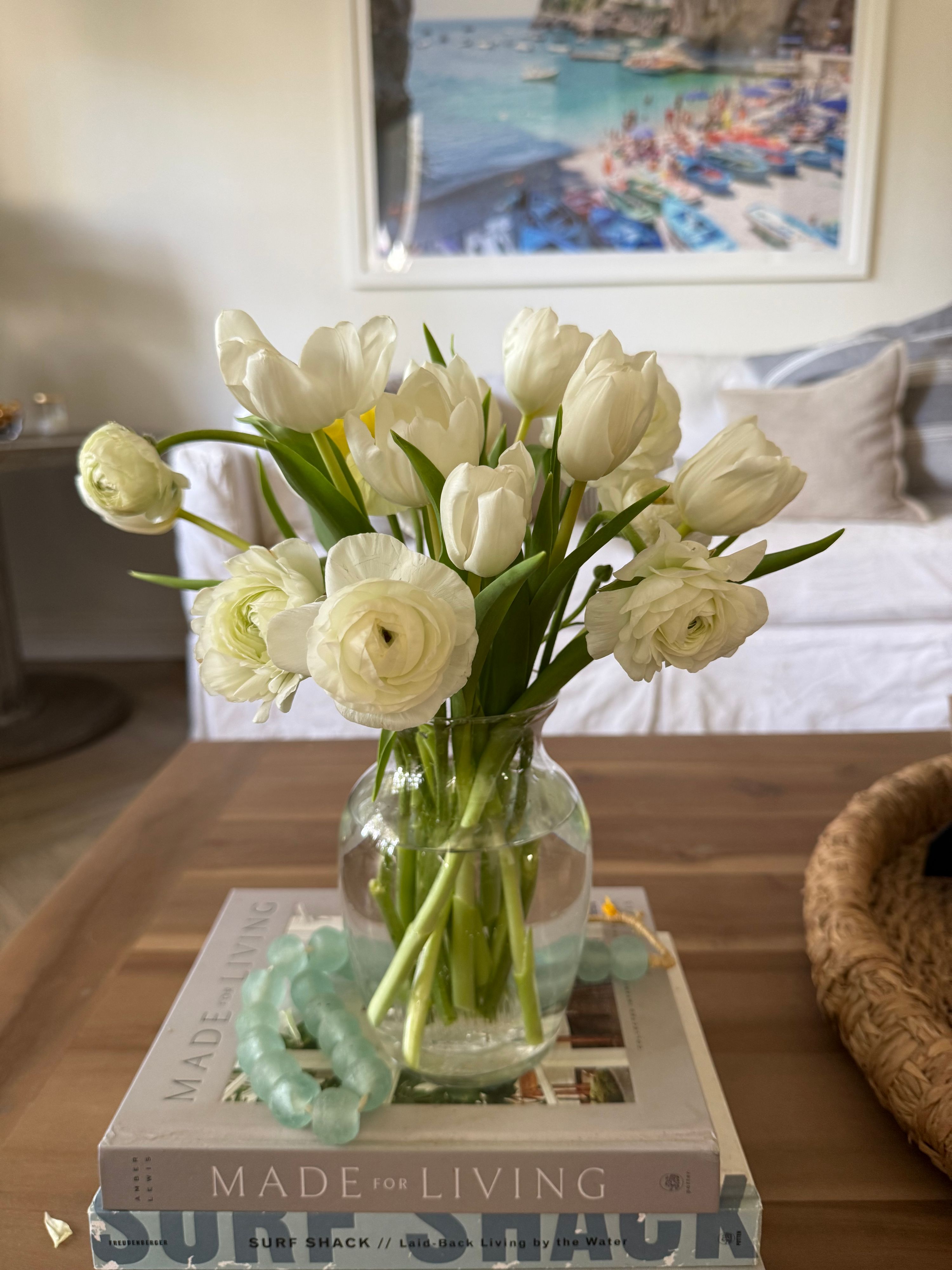 White tulips and ranunculus in a clear glass vase on a coffee table