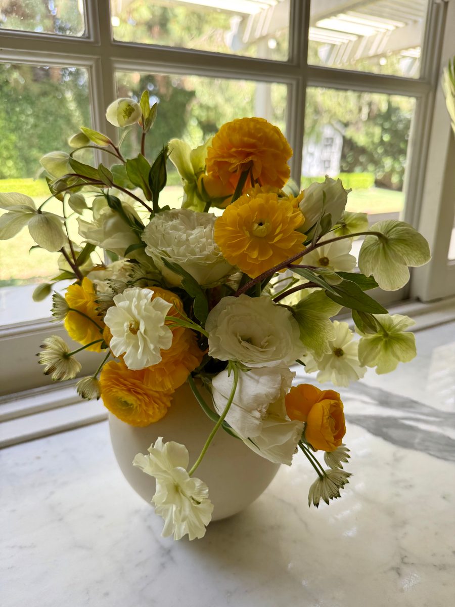 Yellow and white ranunculus with hellebores in a white ceramic vase
