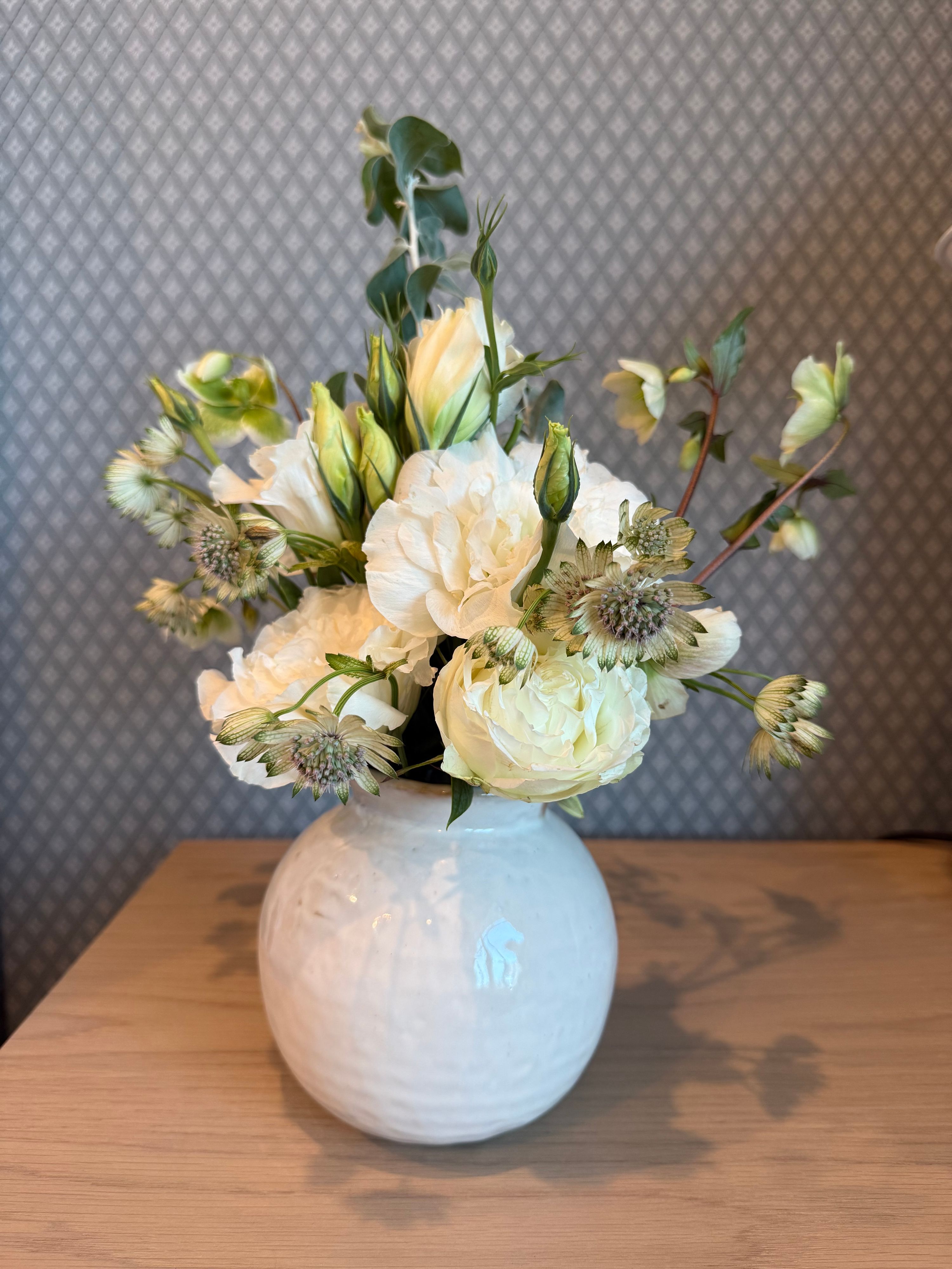 Cream ranunculus and lisianthus with eucalyptus in a white textured vase