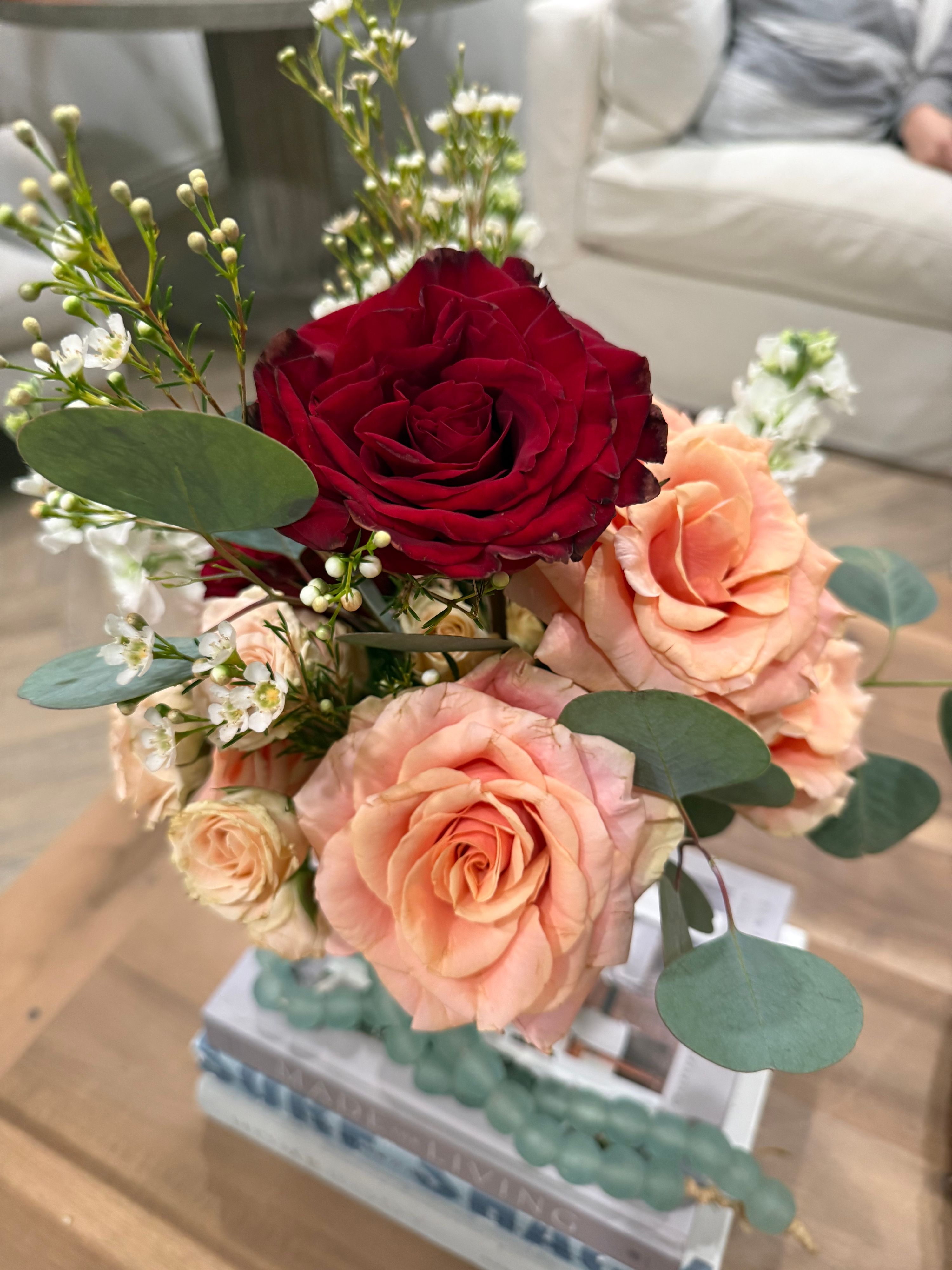 Deep red rose with peach roses, white stock and eucalyptus in a glass cube