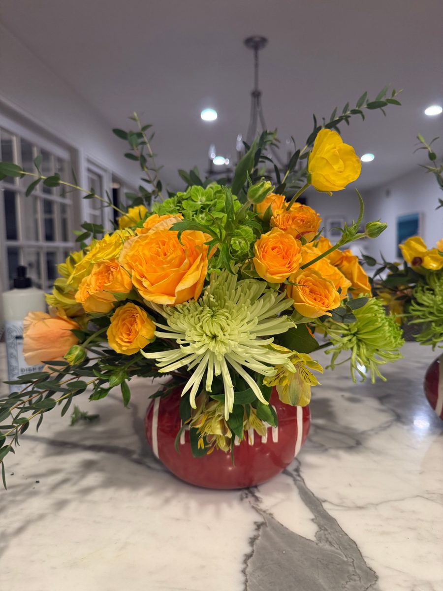 Orange spray roses and green spider chrysanthemums in a red ceramic vase