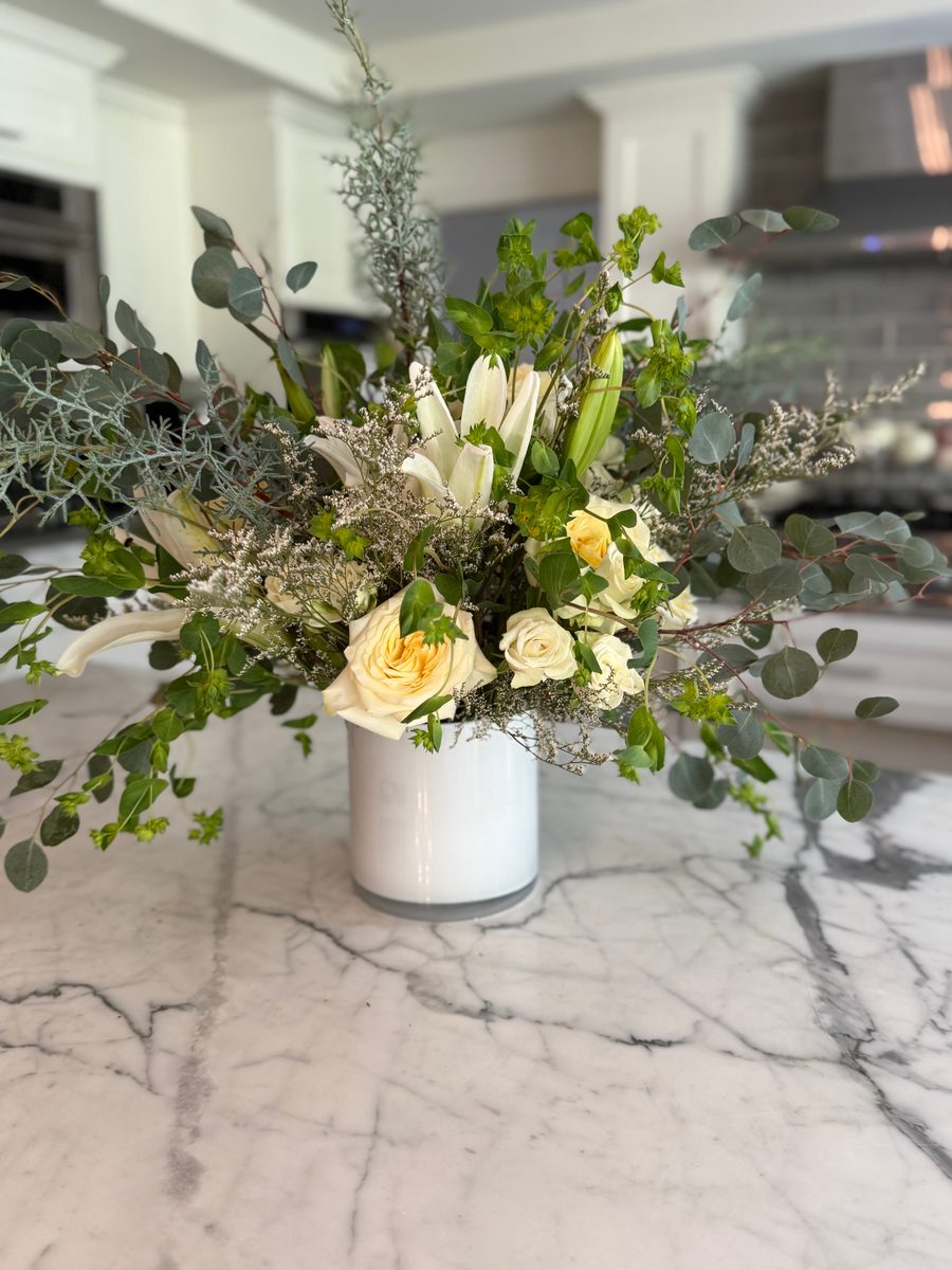 Cream roses and white lilies with eucalyptus in a white cylinder vase