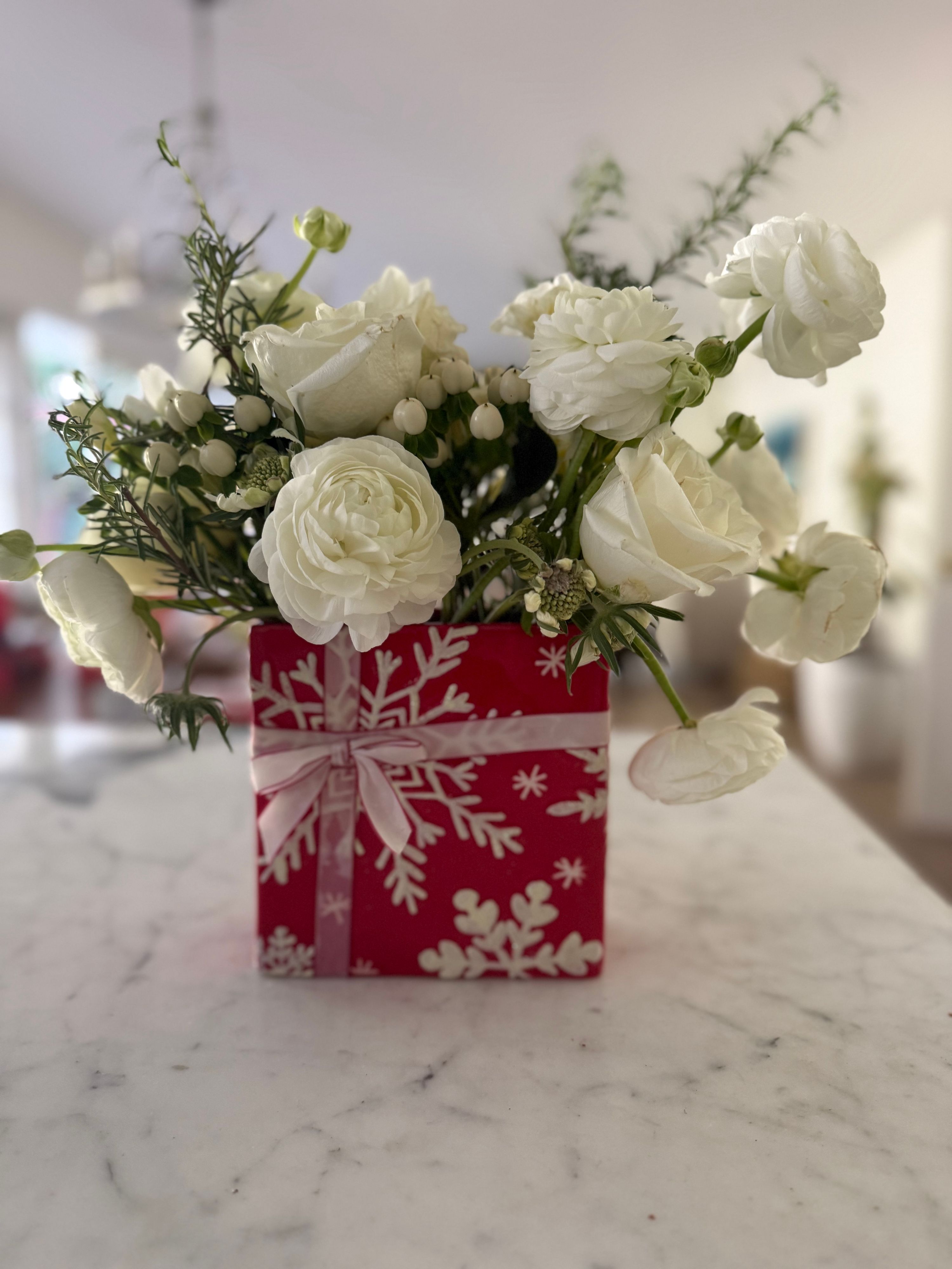 White ranunculus and roses arranged in a red snowflake holiday gift box