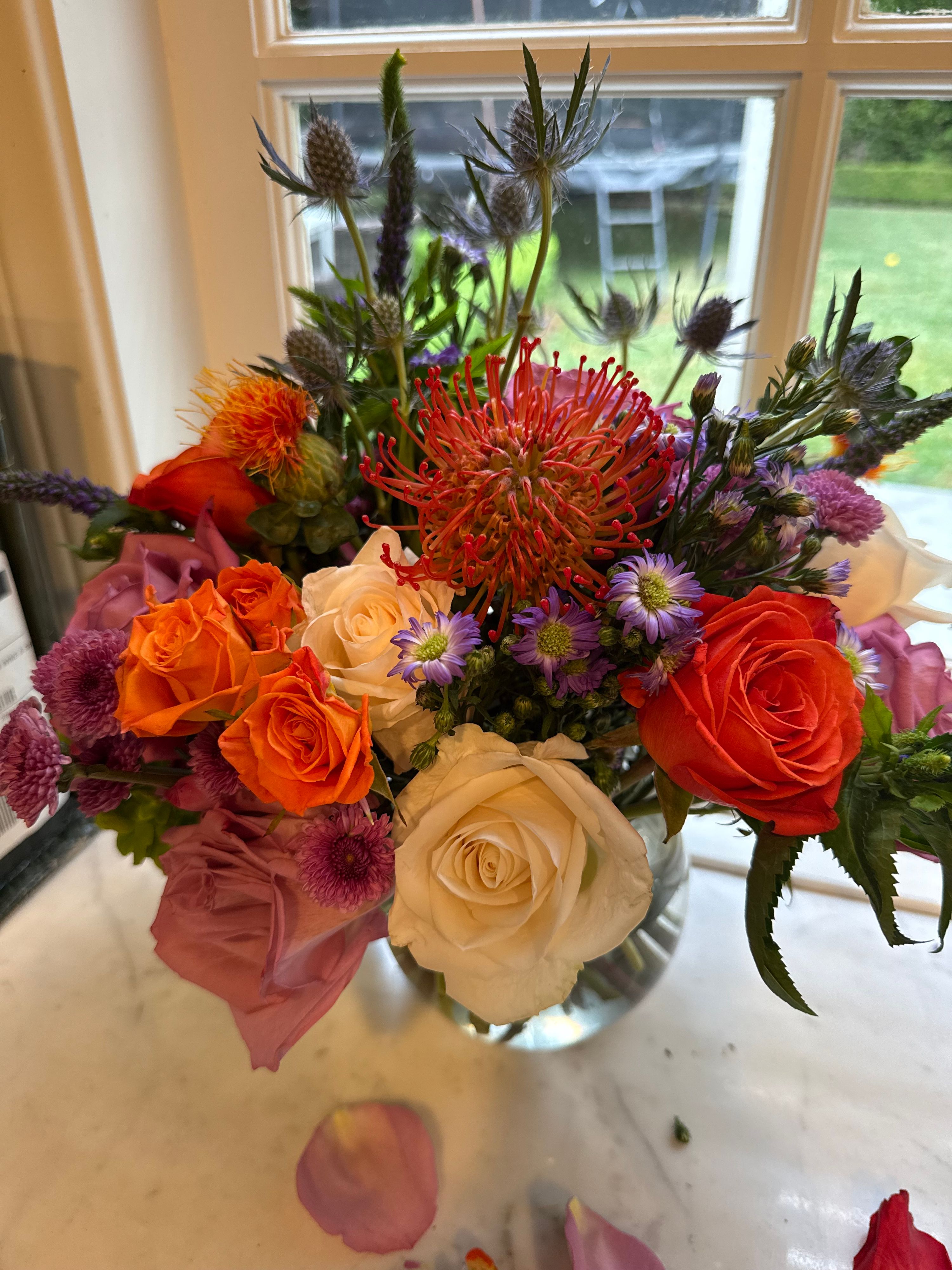 Orange, cream and purple arrangement with roses, pincushion protea and thistle