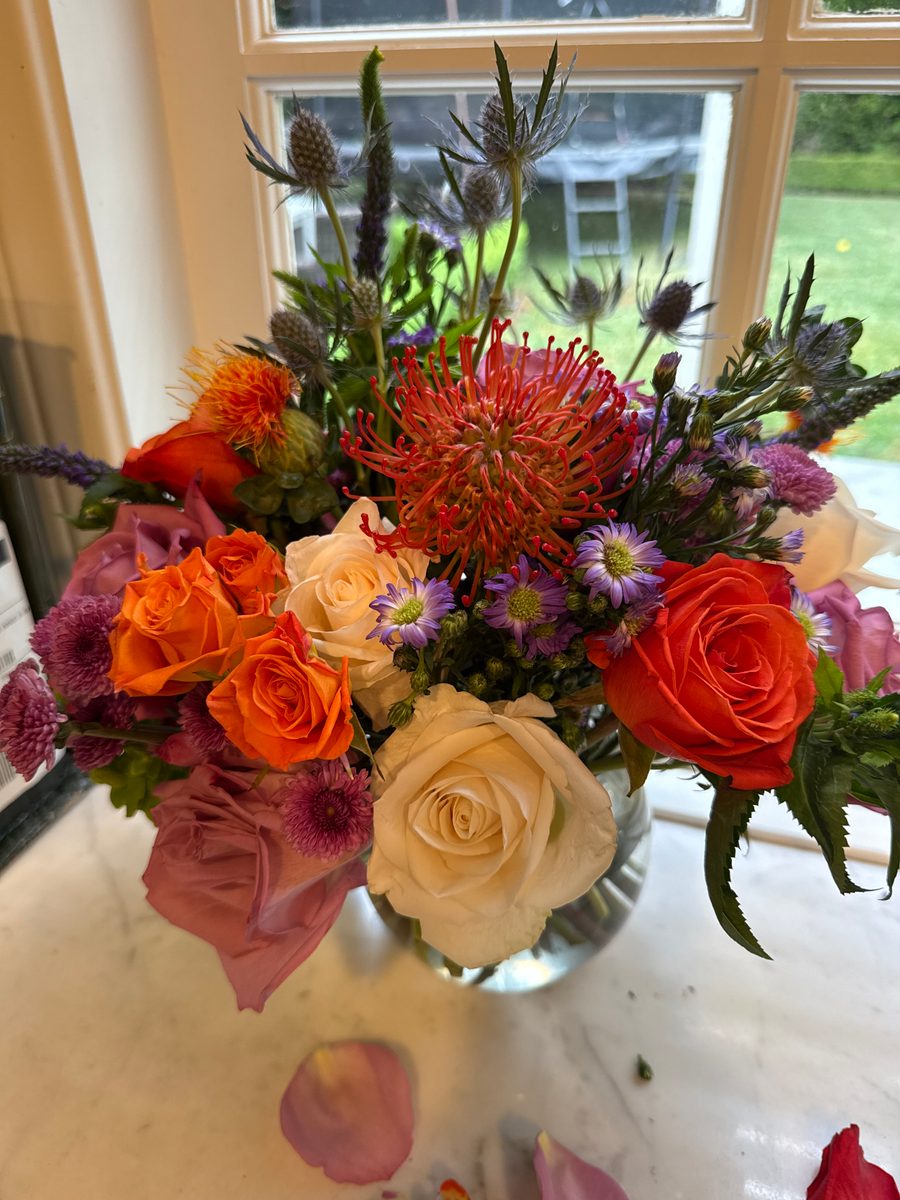 Orange, cream and purple arrangement with roses, pincushion protea and thistle