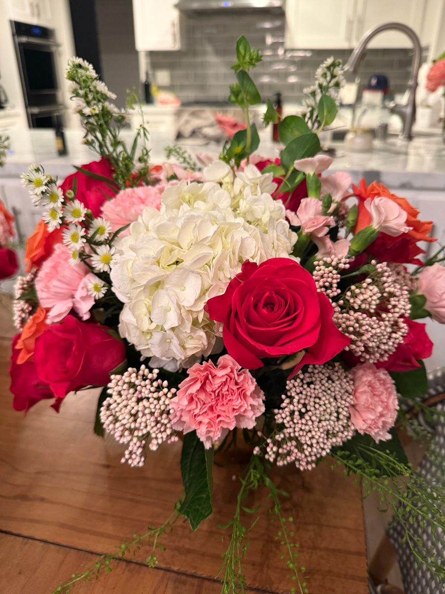 White hydrangea with red and pink roses and carnations in a glass vase
