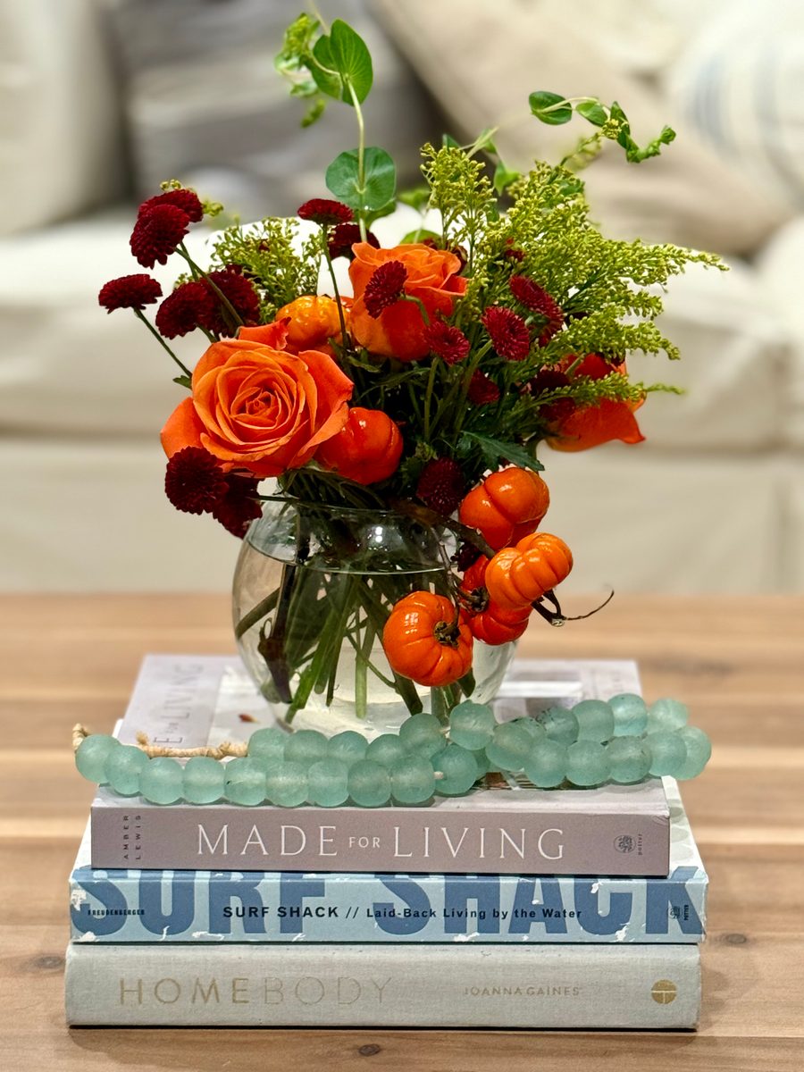Orange roses and ranunculus with mini pumpkins in a glass vase