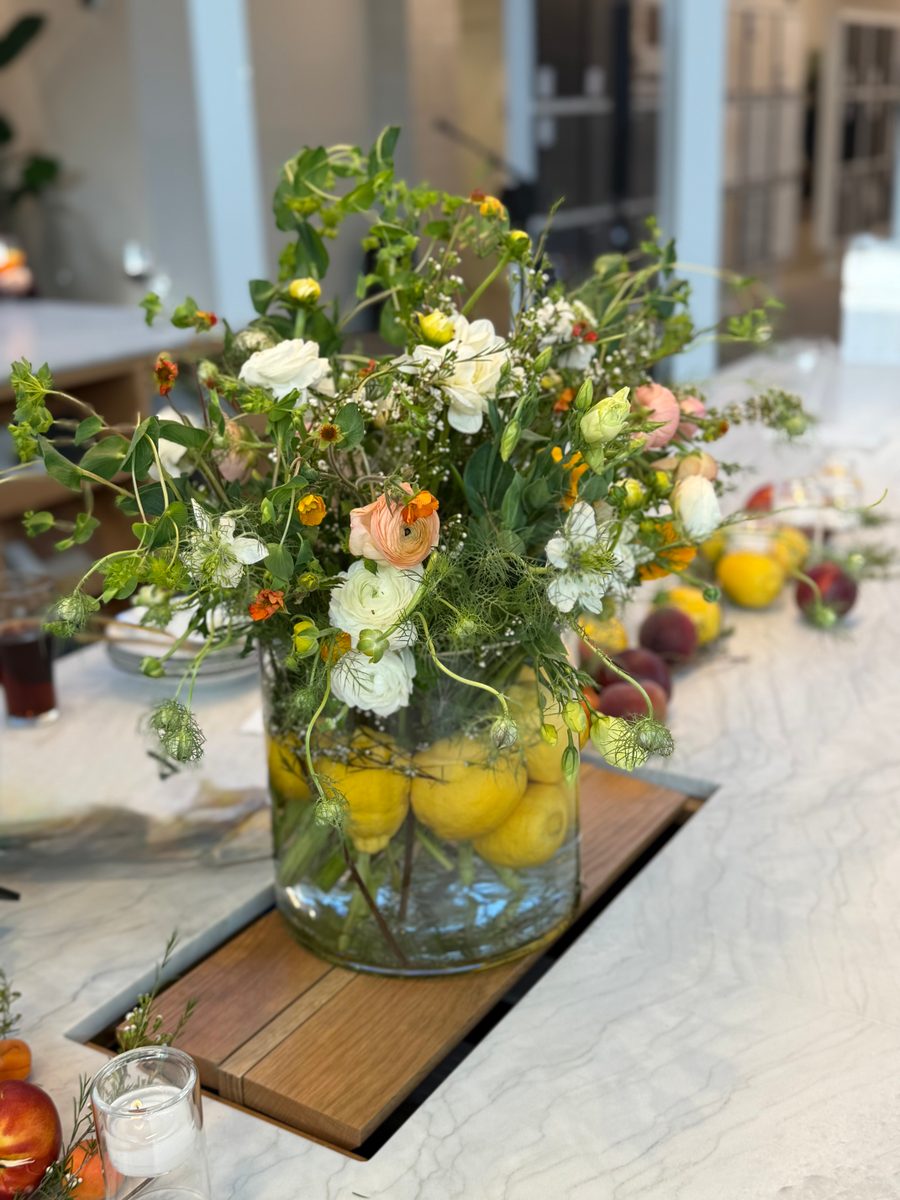 Peach and white flowers above whole lemons in a clear glass vase