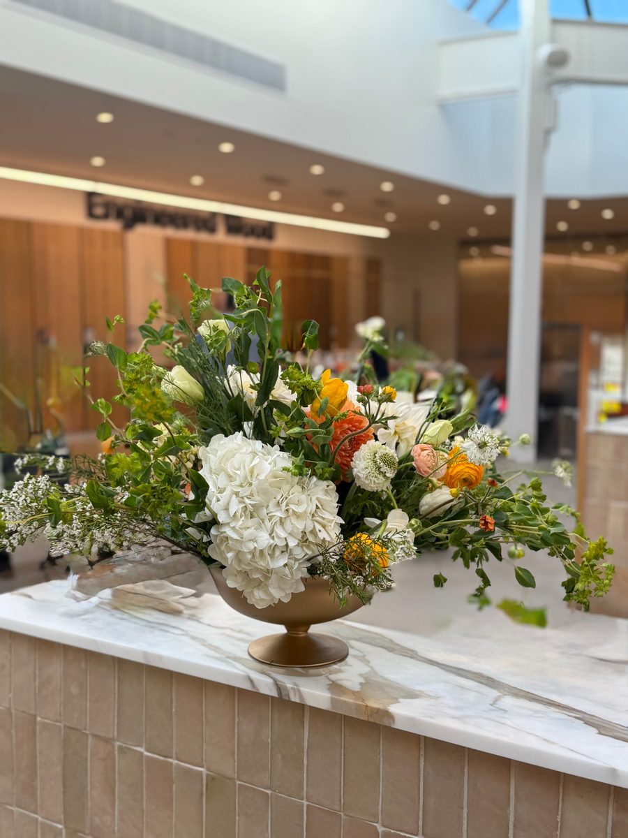 White hydrangea and orange ranunculus in a gold compote on a lobby counter