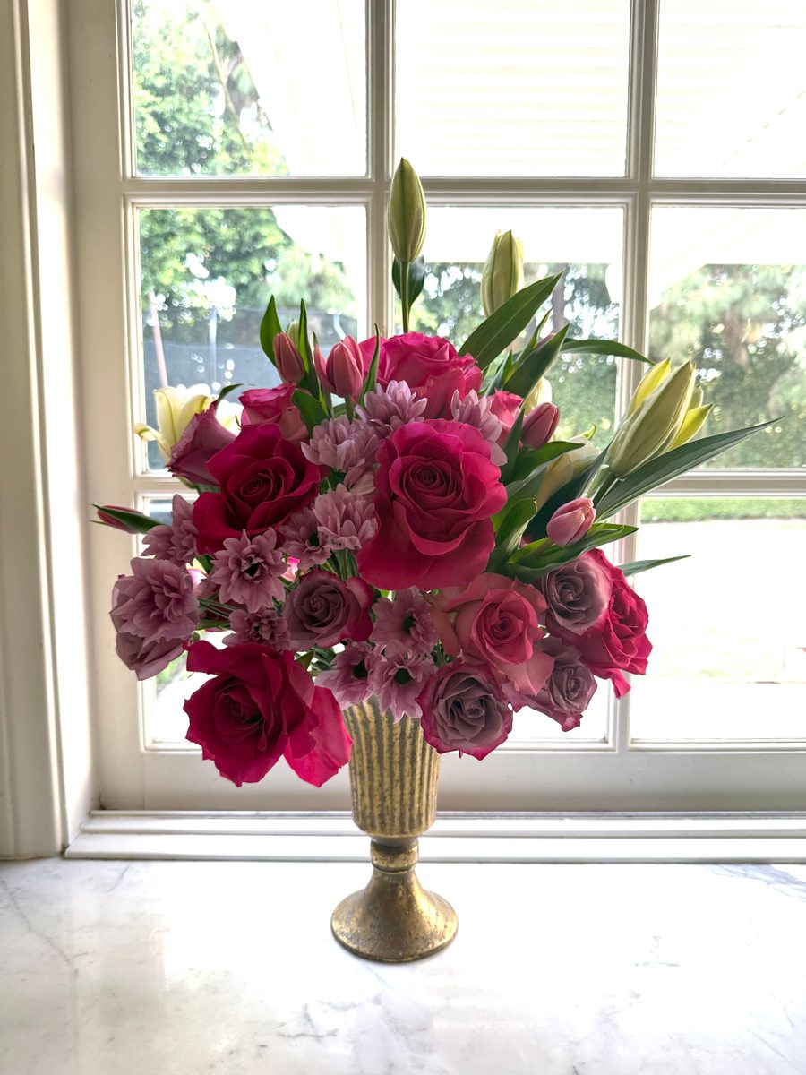 Magenta roses, lavender spray roses and pink lilies in a gold footed vase